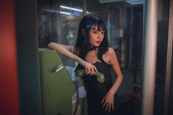 一位身穿黑色连衣裙的年轻女子拿着一个绿色瓶子摆姿势