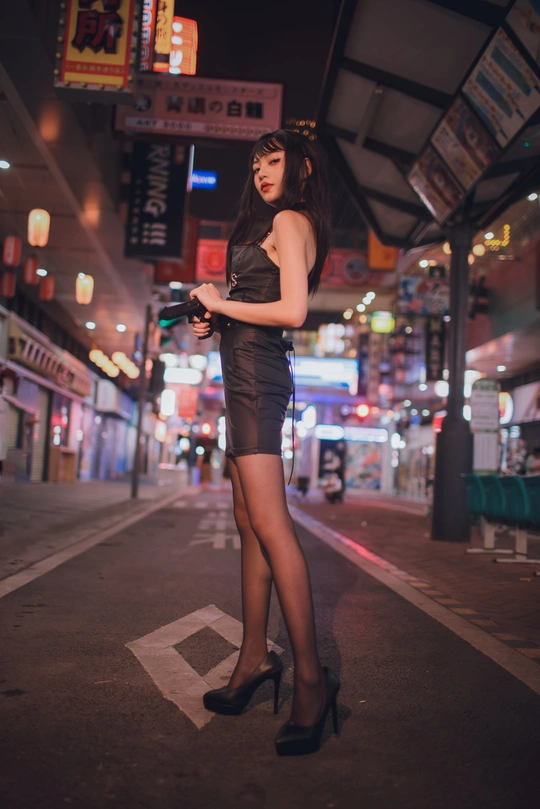 一个穿着黑色连衣裙和高跟鞋的年轻女子晚上站在城市街道上