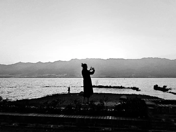 一张黑白照片 一对男女站在水边 背景是山脉。