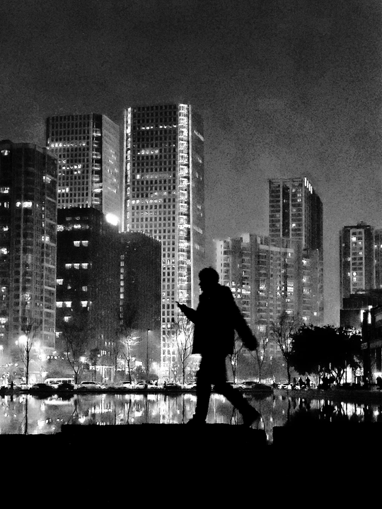 一张黑白照片 一个夜晚在城市的男人带着伞行走。