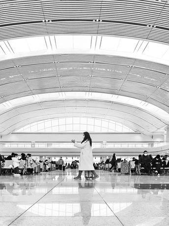 一张黑白照片 机场航站楼 有人走动 一位穿大衣的女人站在行李旁