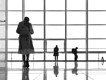 一个人站在一栋建筑的大窗户前 周围有人注视着他 他的轮廓是黑白的。