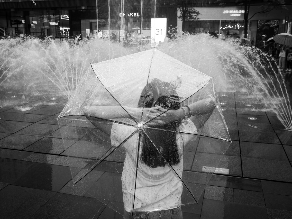 一张黑白照片 一位女士站在喷泉前拿着打开的雨伞。