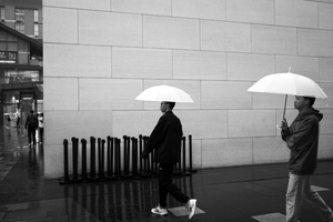 一些男人拿着白伞在雨中走人行道