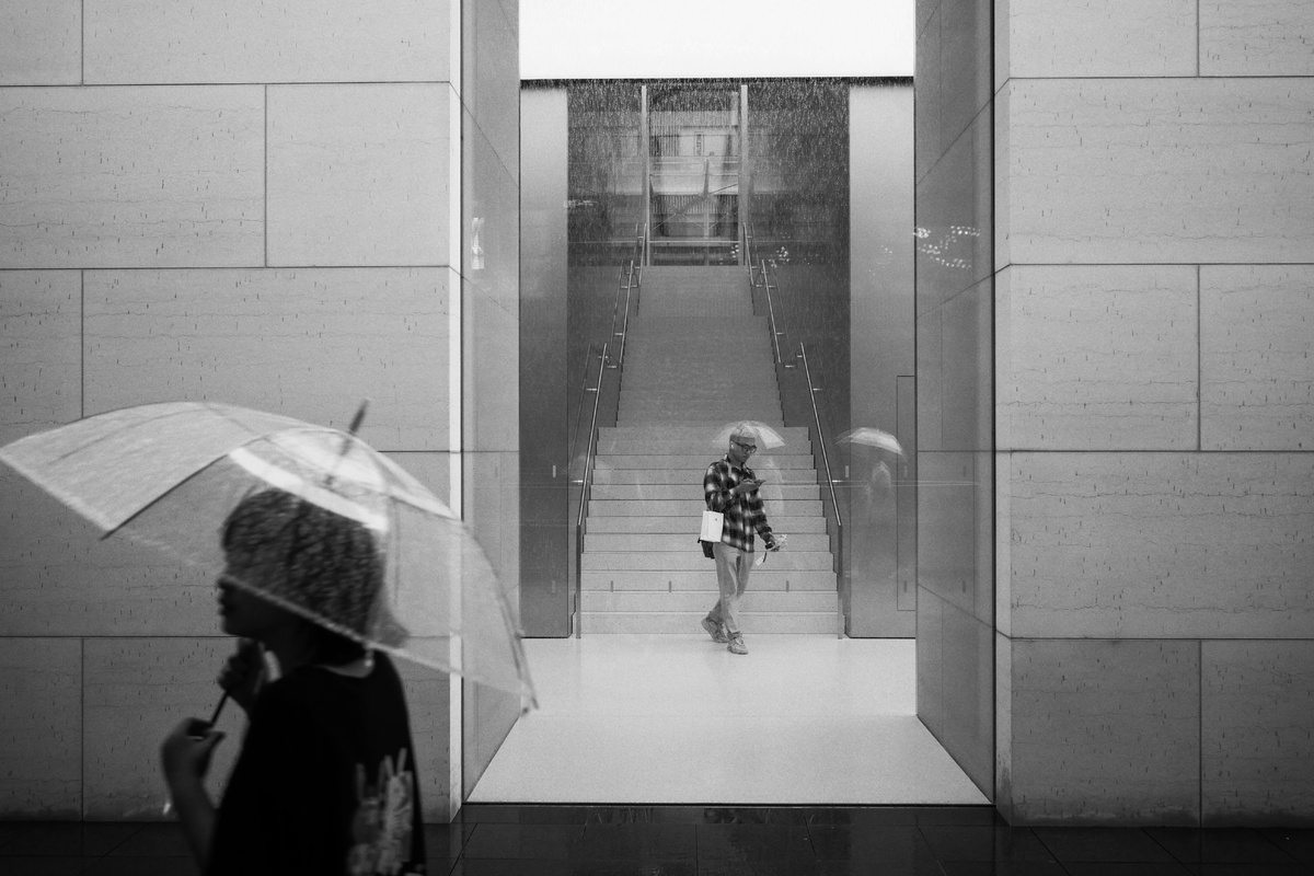 黑白照片 一位女士拿着透明的雨伞 一位小女孩站在一所建筑物里下雨。