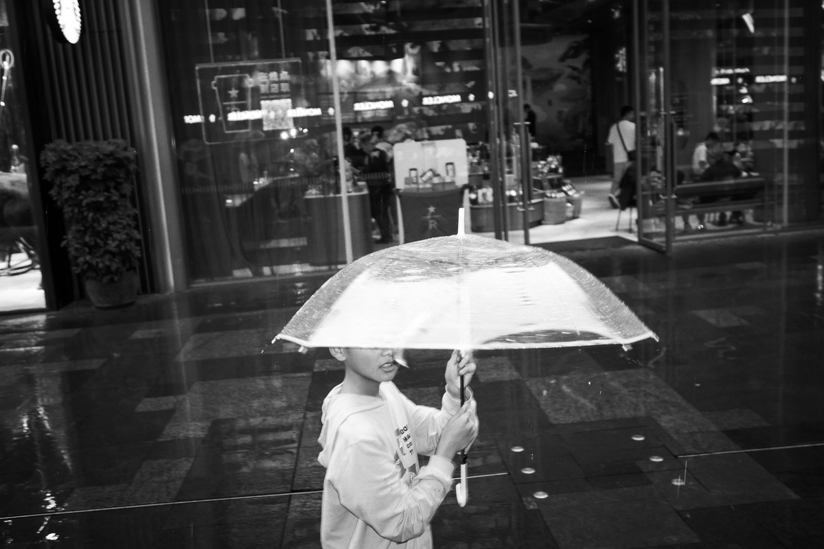 一张黑白照片 一位女士站在雨中 手中撑开了一把伞。
