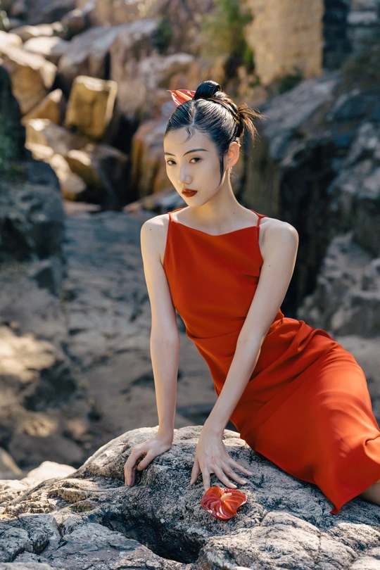 一位穿着橙色连衣裙的年轻女子坐在海滩上的岩石上