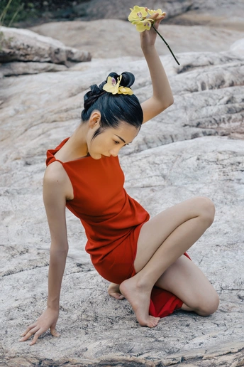 一位穿着红裙子的年轻女子手里拿着一朵黄色的花 坐在岩石上。