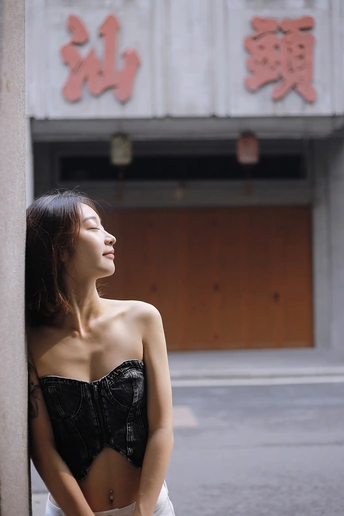 一位穿着黑色衣服的年轻女子靠在一栋街道上的建筑上