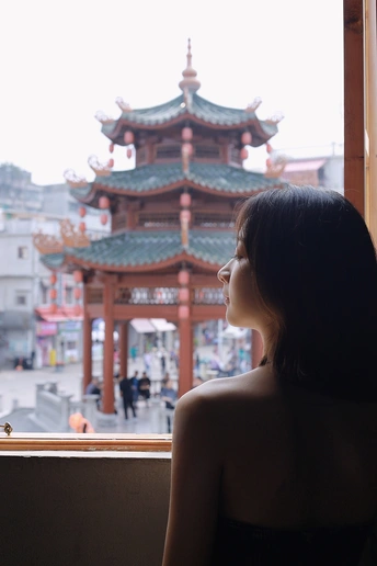 一位年轻女子坐在窗前 凝视着城市中的佛塔。