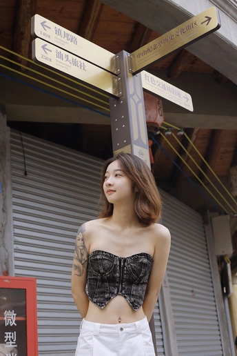 一位穿着上衣和裤子的年轻女子站在街标下