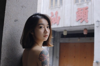 一位有纹身的年轻女子靠在一栋建筑物的墙边