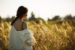 日落时分 一位身穿白色毛衣的年轻女子站在高高的草地上