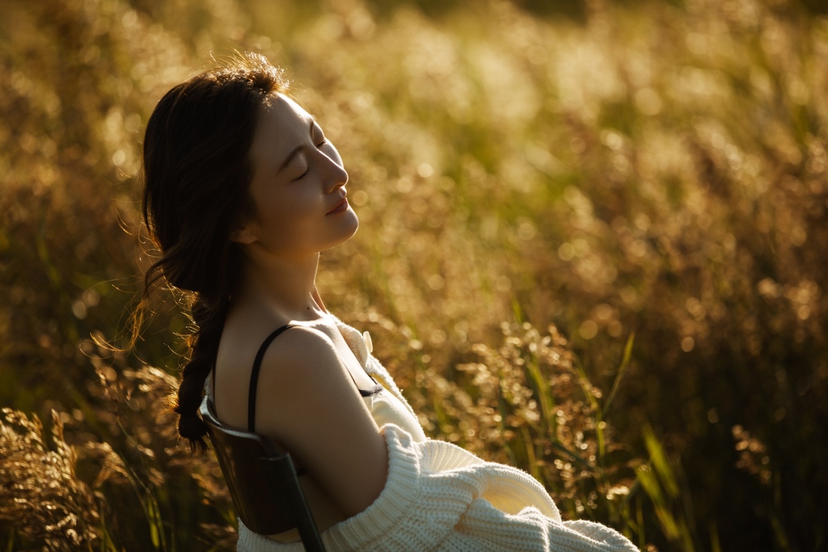 日落时 太阳照耀着一位穿着连衣裙的年轻女子 她坐在一片高高的草地上