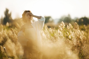 穿着连衣裙的美丽年轻女子在阳光下穿过麦田