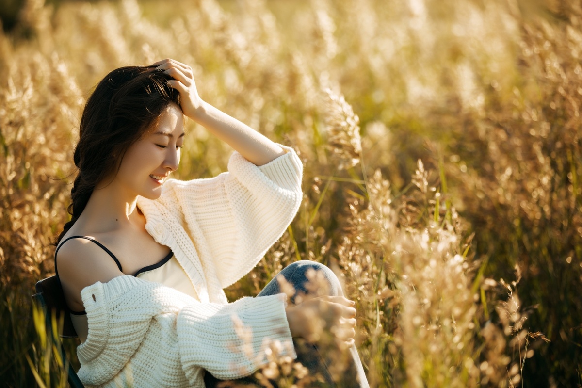 一个穿着白色毛衣的年轻女子坐在高高的草地上