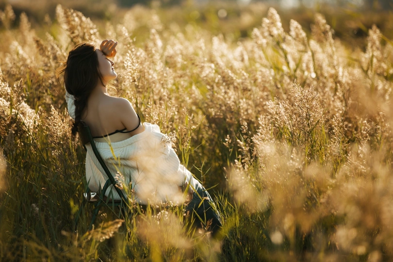日落时 年轻漂亮的女人坐在高高的草地上的椅子上
