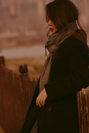 一位年轻女子穿着黑色外套和围巾站在围栏旁边