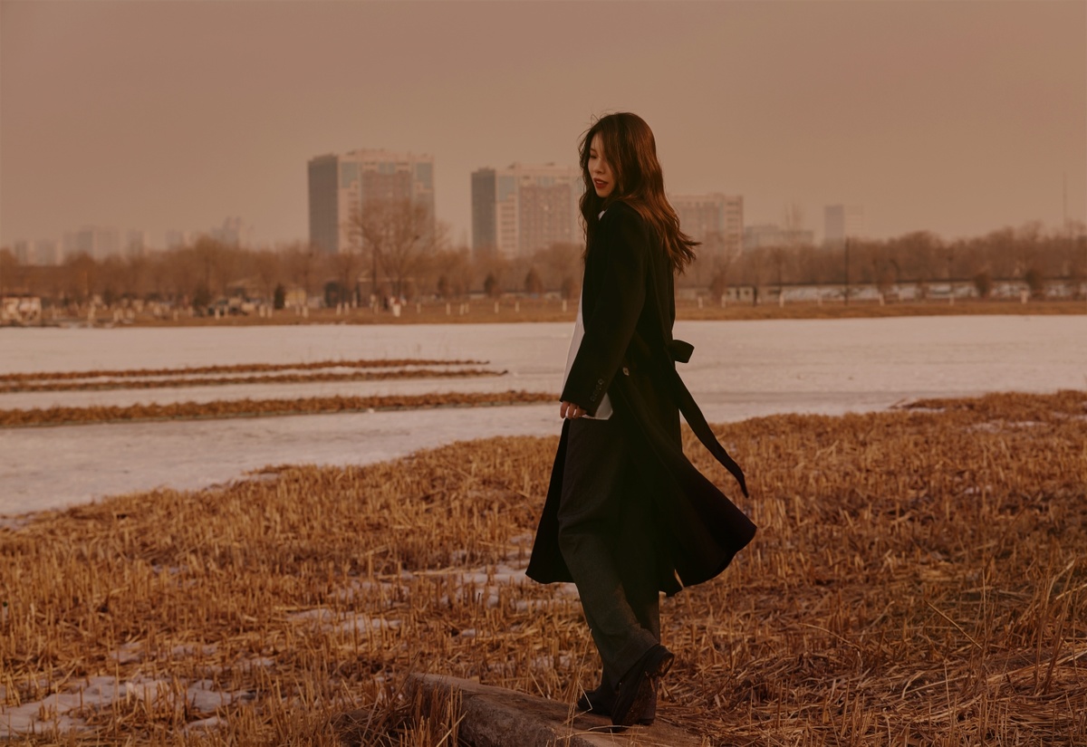 一个穿黑色外套的女人站在水边的一个田地里