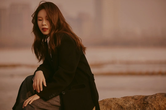 一个穿着黑色外套的年轻女子坐在靠近水边的一块岩石上