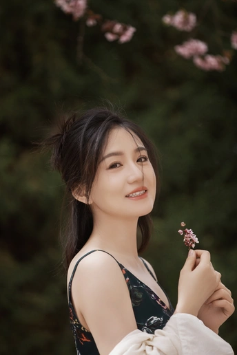一位穿着白色连衣裙的年轻女子为肖像摆姿势 手里拿着一朵花。