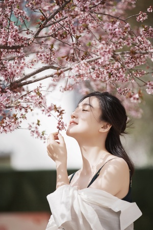 美丽年轻女子抱着花在微风中吹拂 在盛开的花树下