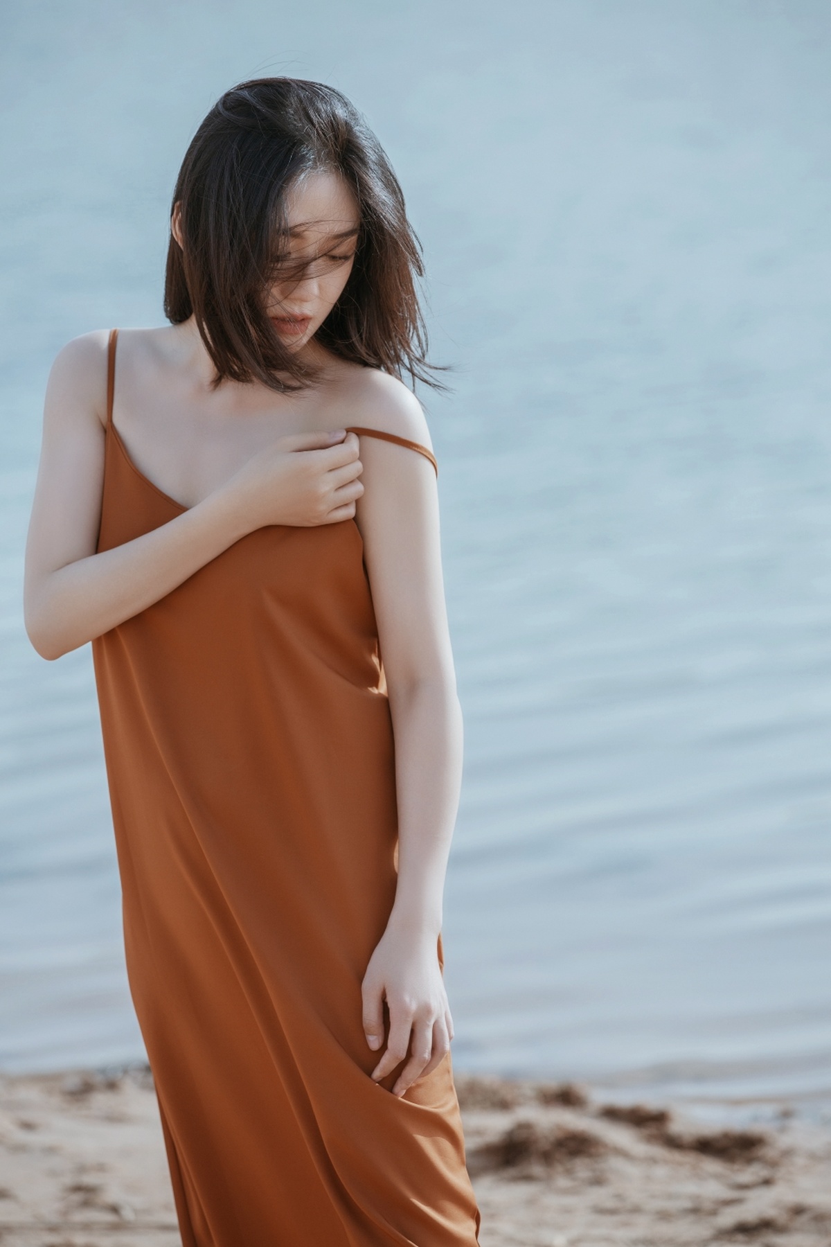 一位穿着橙色连衣裙的年轻女子站在靠近水的沙滩上
