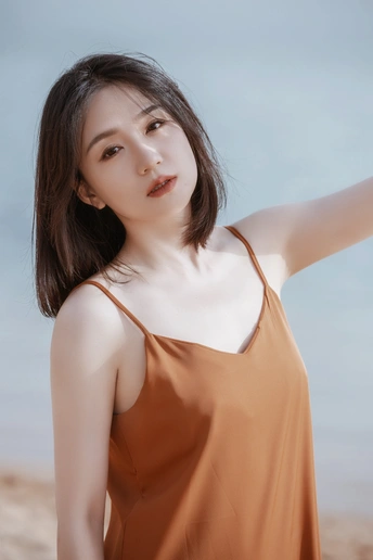 美丽的年轻女子穿着橙色裙子站在海滩上 双手举过头顶