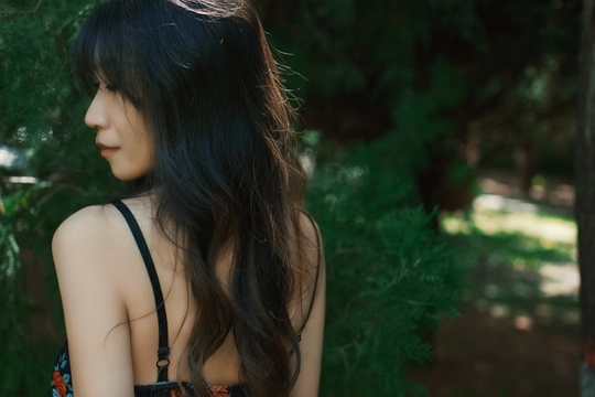 一位长发着黑色连衣裙的年轻女子站在森林中