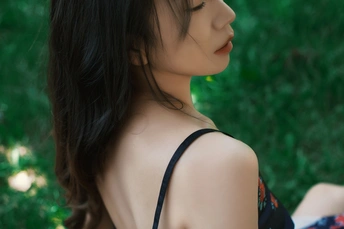 一个穿着黑色连衣裙的年轻女子坐在草地上抬头看