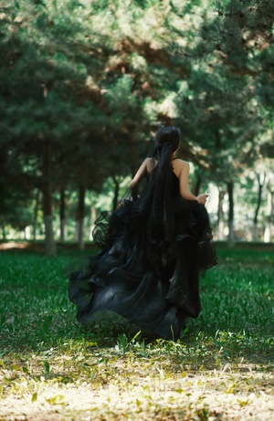 一位穿着黑色长裙的女孩穿过一排树木。