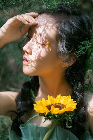 一位年轻女子举着黄色的花挡在脸前 身处绿色的森林中。