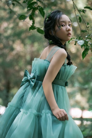 一位穿着绿色连衣裙的年轻女孩在树木丛生的森林中。