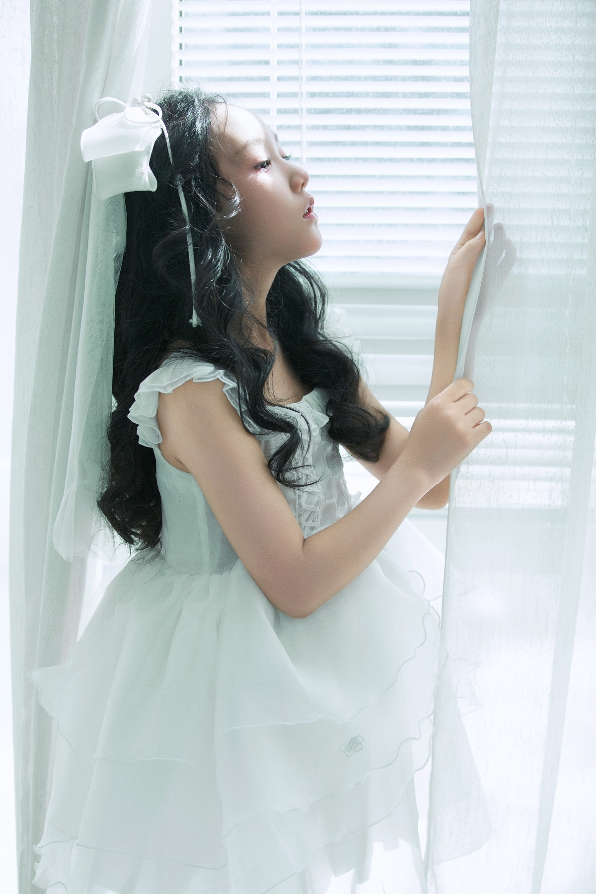 一位穿着白色连衣裙的年轻女子正在窗户旁向外看