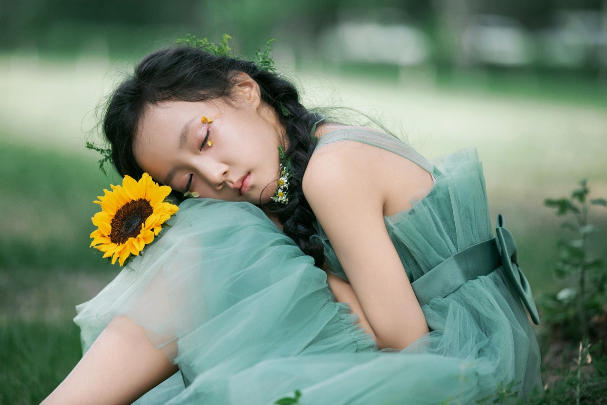 一个穿着蓝色裙子的年轻女孩躺在绿色的草地上 带着向日葵。
