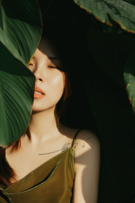 一位美丽的年轻女子站在植物的绿色叶子后面摆姿势