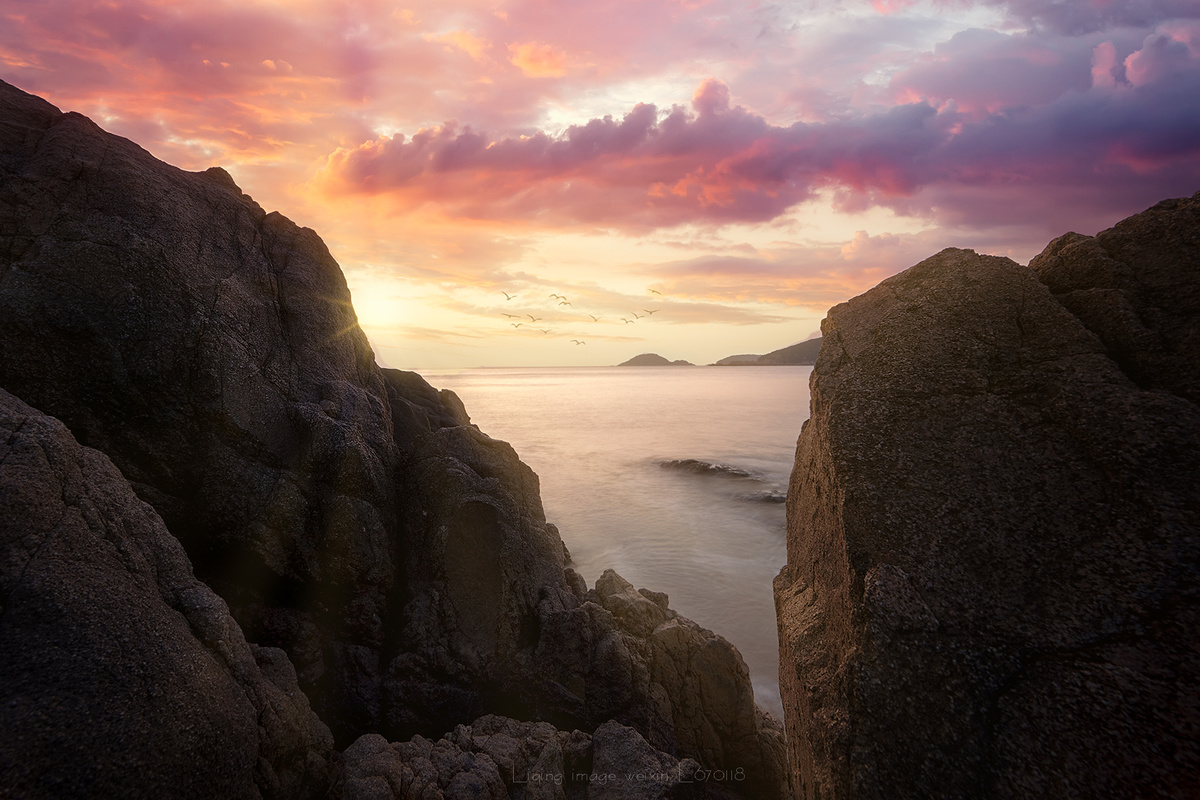 从前景是岩石和悬崖的岩石海滩俯瞰水体或海洋的日落或日出
