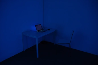 一个黑暗的房间 墙上有一面蓝色的墙 角落里有一张小白的桌子 桌子上放着一台电脑。