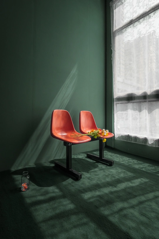 一把红色的椅子坐在一个有花的桌子旁边 这个房间有绿色的墙壁。