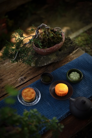 一小锅食物放在木桌上 旁边是一株盆栽植物和一个盘子 盘子上有一个橙子