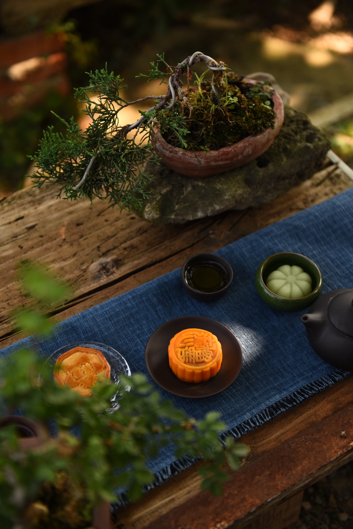 一张木桌 木凳上放着一壶茶、一株小植物和一盘食物