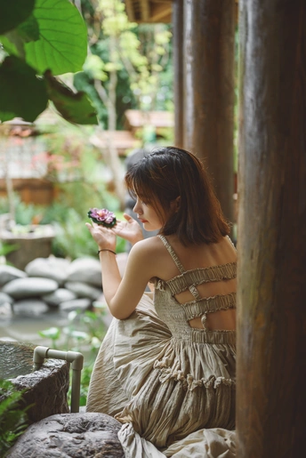 一个穿着连衣裙的年轻女子手里拿着一朵花坐在花园里