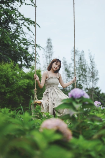 美丽的年轻女子穿着白色裙子在花园里荡秋千