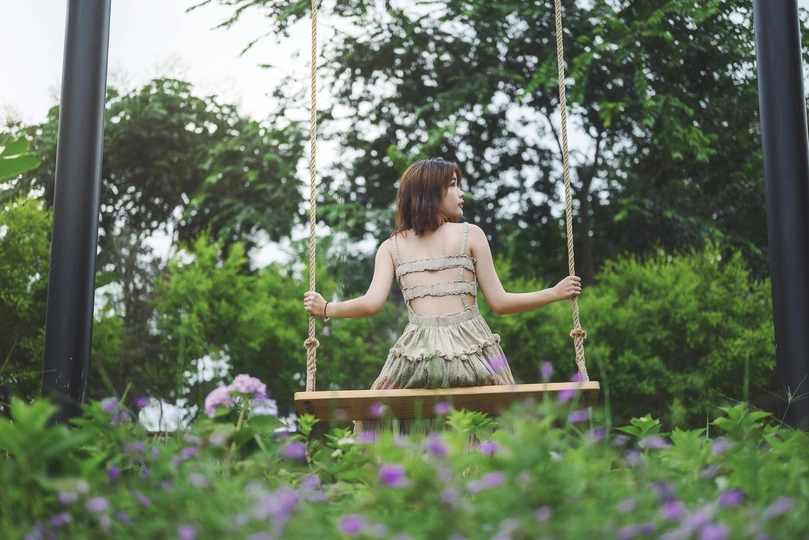 一个穿着连衣裙的年轻女子坐在花园里的秋千上