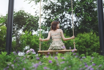 一个穿着连衣裙的年轻女子坐在花园里的秋千上