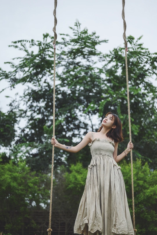 一位年轻女子在树上挂着的一架秋千上荡漾。