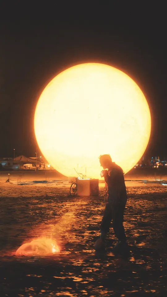 一个人在太阳前面的大型球状物前面的沙滩上溅水