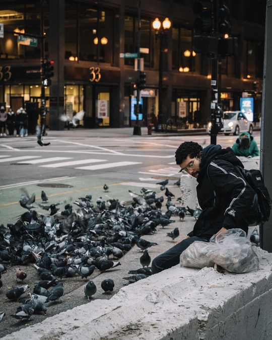 一个人坐在鸽子环绕的 ledge 上 位于城市人行道上 拿着一个袋子。