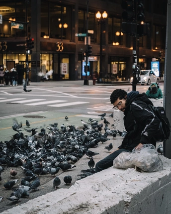 一个人坐在鸽子环绕的 ledge 上 位于城市人行道上 拿着一个袋子。