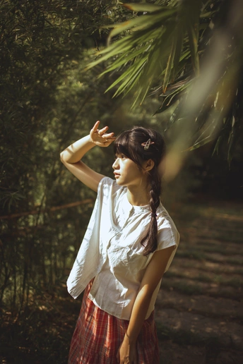 一位年轻女子站在森林中 手伸向一棵树。
